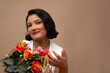 © AnaRosa - Elegant woman in white dress holding colorful roses, looking at camera. Horizontal studio portrait with copy space on brown background. Feminine style, ideal for beauty, valentine's day, mother's day.