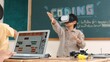 © InfiniteFlow - Asian boy wearing VR headset to enter metaworld at table with electronic board while girl coding system. Group of diverse student working together to develop program and writing code. Pedagogy.
