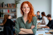 © GraysonStock - A young businesswoman standing with her arms crossed in an office, smiling in a business meeting.