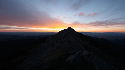 Poster - A dramatic sunset over a mountain ridge. The sky is filled with vibrant orange and purple hues. The silhouette of the mountain creates a stark contrast against the colorful sky