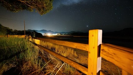Fototapete - Night landscape with a wooden fence in the foreground. Milky way and stars with trees and mountains in the background creating a scenic atmosphere
