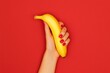 © Oulaphone - A woman hand with red nail polish holding a banana against a red background. A bold and sensual visual concept symbolizing femininity and provocative contrast.