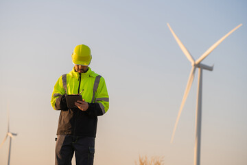 Fototapete - Engineer man working with tablet at windmill farm Generating electricity clean energy. Wind turbine farm generator by alternative green energy.