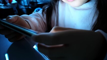 Young child using a smartphone in a darkened room, the screen illuminates the face of the little girl, digital entertainment, online games
