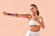 © HBS - A sporty fitness girl, a trainer, is stretching her arms using a pink resistance band against a light background in a studio.