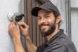 © barmaleeva - Smiling technician installing security camera on house wall