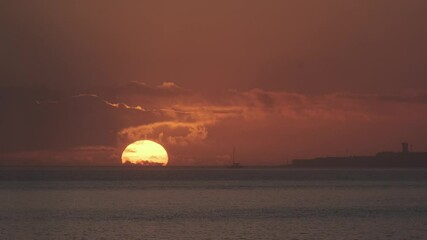 Wall Mural - golden sun setting over a tranquil ocean in portugal, casting warm hues on the water as a sailboat g