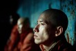 © The Stock Alchemist - Contemplative Monk Portrait: Young Asian Monk in Orange Robe, Side Profile, Textured Blue Background