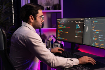 Working smart IT developer analyzing data software development on two pc screen, creating application program updated version online website page system online at neon light cyber office. Surmise.