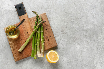 Wall Mural - Wooden board with fresh green asparagus, lemon and glass bowl of oil on grey grunge background