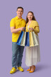 © Pixel-Shot - Beautiful young couple with shopping bags on lilac background