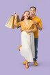 © Pixel-Shot - Beautiful young couple with shopping bags on lilac background