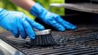 © Udin - Person cleaning a barbecue grill outdoors with blue gloves, surrounded by greenery