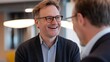 © Adi - Smiling men in business casual attire with glasses engaged in a friendly conversation in a modern office