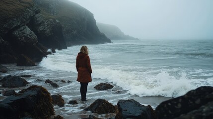 Wall Mural - a solitary figure stands on the rocky shore amid fog. the waves crash softly against the stones. a m
