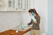 © Studio Romantic - Focused young woman wearing rubber gloves using cup plunger to unclog sink in kitchen while talking on phone. Busy female homeowner calling emergency or plumbing service while solving plumbing issue.