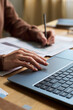 © pressmaster - Vertical shot of hands of young woman calculating expenses using laptop, while sitting at desk and managing budget