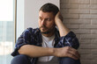 © New Africa - Depressed man sitting near window at home
