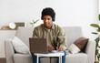 © Prostock-studio - Web-based education concept. Happy teen guy in headset taking notes while communicating online with tutor on laptop. Funky African American adolescent making homework for his online course