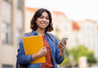 © Prostock-studio - Outdoor Portrait Of Smiling Arab Female Student With Smartphone And Workbooks, Happy Young Middle Eastern Female Using Mobile Phone While Standing Outside At Campus, Resting After Classes