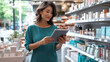 © Katerina Bond - Young female salesperson using digital tablet in her work, in modern cosmetics store, standing near shelves with skin care products, focused and smiling in brightly lit sales area.