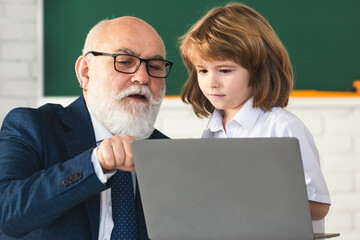 Fototapete - Portrait of senior teacher and school child. Mature teacher helps school child learn. School teacher and child in classroom. Teacher in school on lesson teach child on laptop.