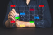 © meeboonstudio - Close-up of hand managing colorful agenda on virtual calendar screen for time management.