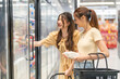 © Art_Photo - Young asian women shopping for dairy products from a refrigerator in grocery store, smiling enjoying healthy lifestyle choices selecting fresh milk together in supermarket chilled section