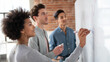 © Anastasia - A multicultural startup team collaborates on a project, with a young Black woman writing on a whiteboard, while two young men, one of Caucasian descent and one Asian, observe thoughtfully