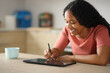 © Antonioguillem - Happy black woman drawing with stylus pen in a tablet at home