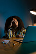© Daniel - Vertical portrait of African American woman working late at night using laptop at home office having headache.