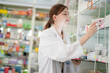 © ultramansk - woman pharmacist wearing lab coat carefully selects medication in a pharmacy. critical role of pharmacists in ensuring patient safety and effective healthcare. female organizes medication on shelves.