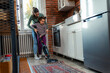 © DusanJelicic - In a cooperative effort, the mother stands beside her child as they vacuum the kitchen area, sharing the responsibility of keeping their home clean.