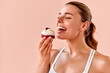 © HBS - A portrait of a delighted girl holding a delicious raspberry dessert, about to take a bite, set against a soft peach background. Temptation and the pleasure of a tasty treat.