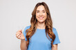 © ViDi Studio - Young smiling woman wearing blue t-shirt casual clothes hold in hand invisible transparent aligners, invisalign dental braces isolated on plain solid white color background studio. Lifestyle concept.