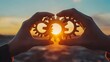 © Anuson - Two hands hold three interlocking gears silhouetted against a vibrant sunset symbolizing teamwork cooperation and success.