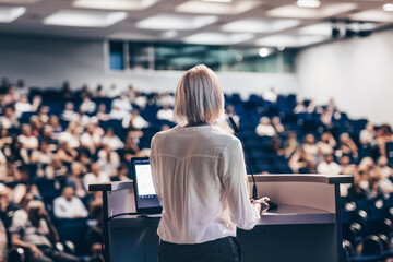 Wall Mural - female speaker giving a talk on corporate business conference. unrecognizable people in audience at 