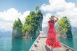 © Vladimir Razgulyaev - A Woman female solo traveler in a Red dress and hat on a Thai boat near the famous Three Rocks site on Cheo Lan Lake in Thailand. Travel and tours to the sea and islands of Thailand and Southeast Asia