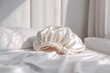 © BYAI - Soft satin shower cap resting on white linens in a serene bedroom setting during morning light
