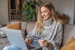 © Desmond - A young White woman sitting on the sofa at home in a living room with a laptop on the lap and holding a credit card. Online shopping, payment, purchase, buy. E-commerce.