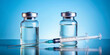 © Roman - Two clear vials with liquid are positioned alongside a syringe on a shiny surface. The soft blue background creates a calm atmosphere, emphasizing the medical setting