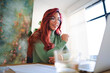 © Studio Marmellata - An Arab woman with red hair works at her laptop. She is smiling and wearing glasses. The natural light illuminates her workspace.
