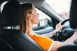 © deagreez - Stylish young woman driving a car during a sunny day in the city, showcasing casual clothing and an upbeat lifestyle