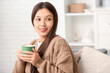 © Pixel-Shot - Beautiful young Asian woman with cup of hot tea in living room