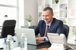 © Pixel-Shot - Portrait of handsome mature businessman working with laptop at table in office