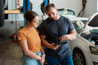 © peopleimages.com - Customer, diagnostic and tablet with mechanic in garage for inspection, maintenance or vehicle service. Woman, quotation and car as auto repair in workshop for engineering, test and motor performance
