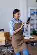 © David - Portrait of Asian female small businesses SME entrepreneur usephone working at home, online marketing, packing boxes, SME sellers, concept, e-commerce team, online sales.