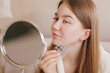 © st.kolesnikov - Girl examines face in mirror while holding pimple patch sheet for skincare treatment.