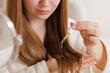 © st.kolesnikov - Girl using dropper to apply yellow oil to hair tips during self-care and treatment at home.