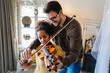 © NDABCREATIVITY - Music is so much fun. Young father teaching his little daughter to play violin and smiling.